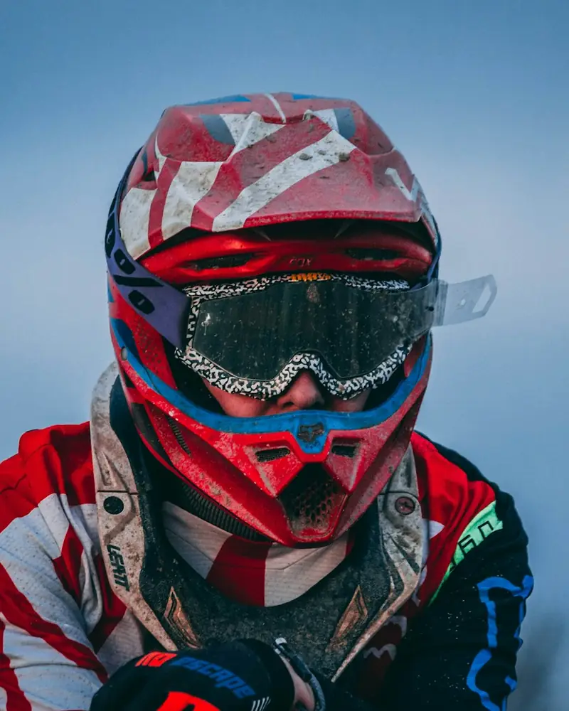 Piloto com capacete vermelho, óculos com lama e roupa de motocross